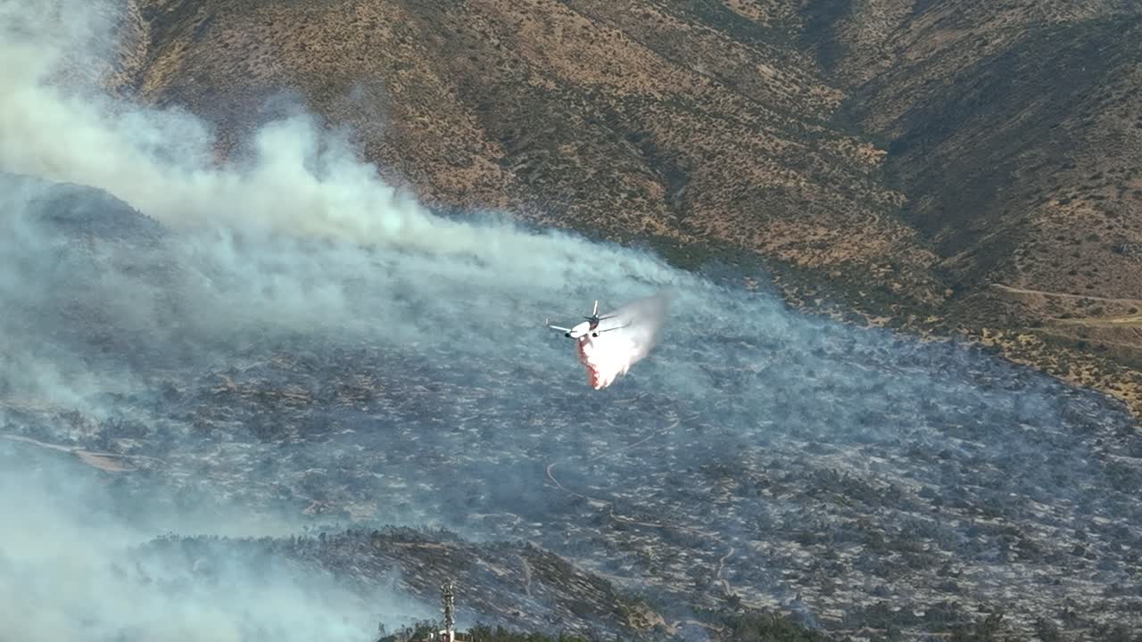 Avión cisterna lanza retardante de fuego sobre un incendio forestal en montañas áridas
