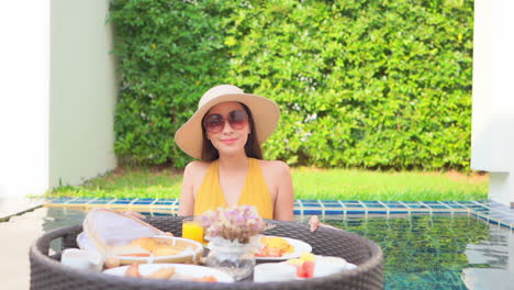 smiling exotic woman with breakfast on floating plate in swimming pool of luxury private villa in tropical destination, slow motion