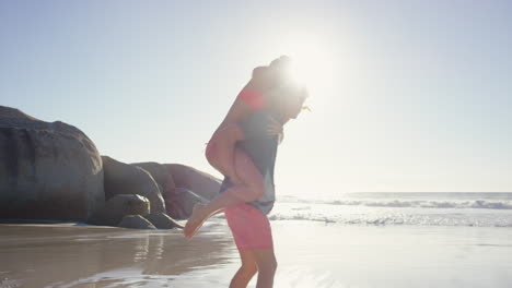 Attractive-man-giving-girlfriend-piggyback-couple-enjoying-nature--on-the-beach