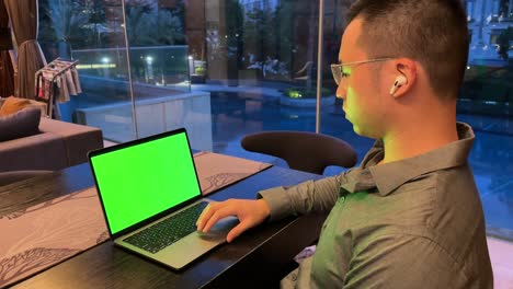 hombre millennial asiático rico desplazamiento portátil con pantalla verde dentro de casa de lujo