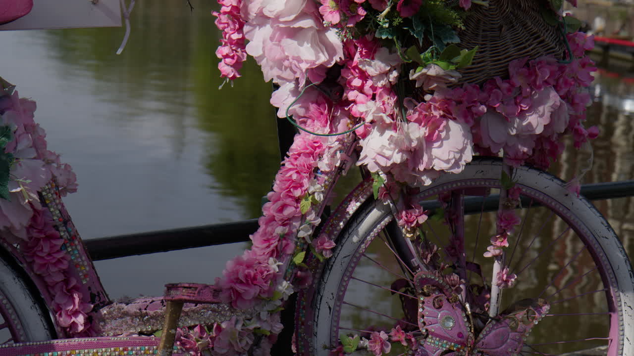 Old Bicycle Covered With Artificial Pink Flowers And Butterfly In Amsterdam, Netherlands. Close-up shot