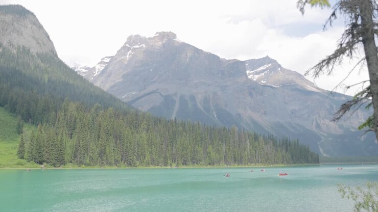 Vista dalla riva del Lago Smeraldo di turisti che vanno in canoa sul lago e bellissime montagne glaciali e foreste sullo sfondo.