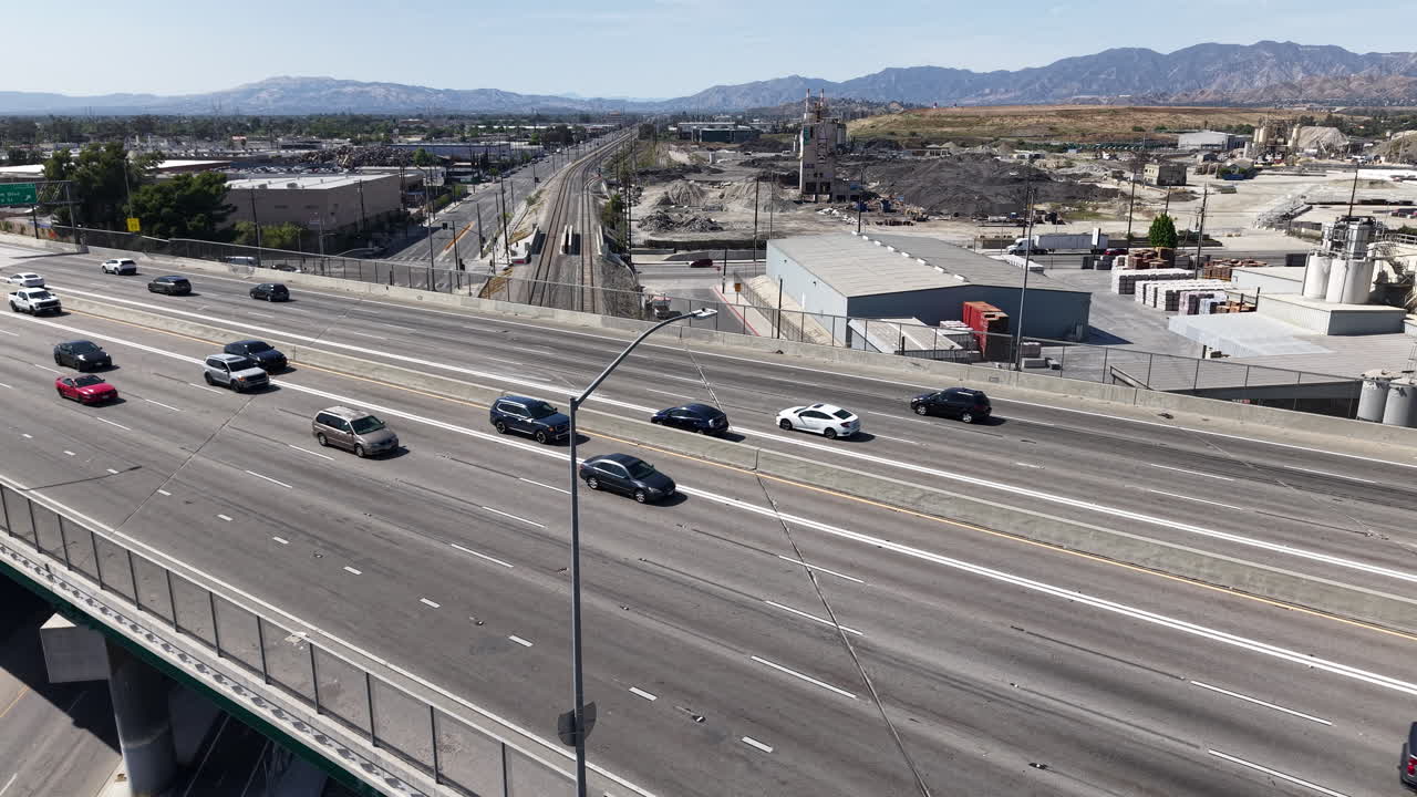 Rekaman drone udara sinematik siang hari yang diambil melayang di samping Jalan Tol 5 di Los Angeles, menunjukkan kendaraan melaju kencang di sepanjang jalan raya