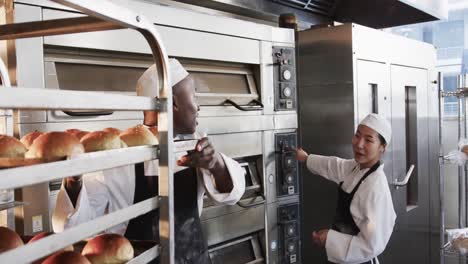 felices panaderas y panaderos diversos trabajando en la cocina de la panadería, horneando rollos en el horno, cámara lenta