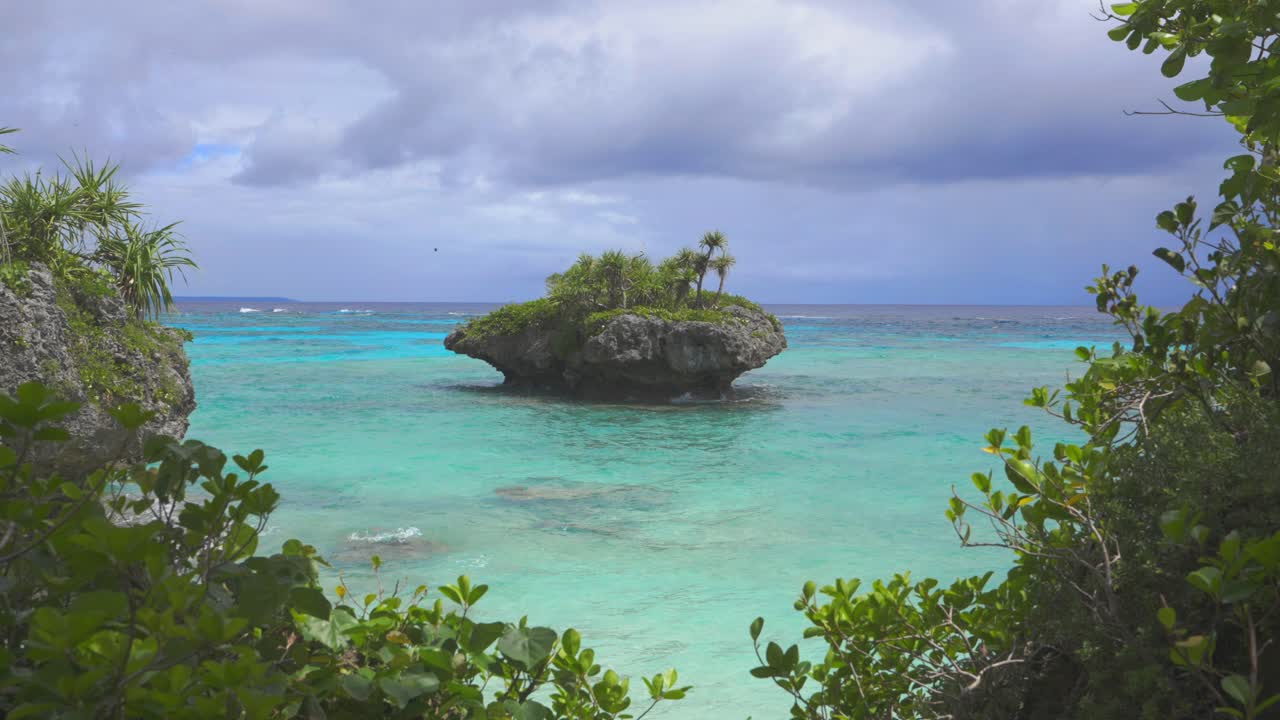 A small rocky island, with its rugged and textured surface, sits majestically in front of a tropical beach, surrounded by crystal-clear waters