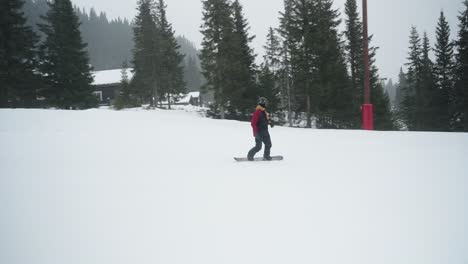 seguimiento en 4k de un hombre en snowboard en un parque divertido haciendo trucos deslizándose en una caja y saltando 180 grados en una colina nevada en un día nublado en una estación de esquí en noruega