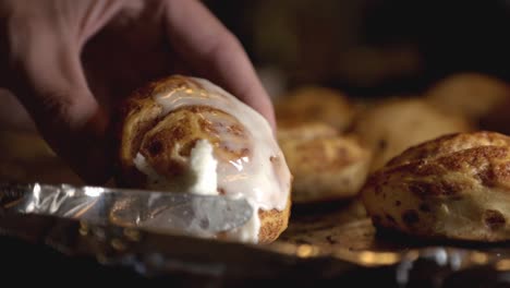 spreading white icing on top of a cinnamon bread with a bread knife - close up slowmo