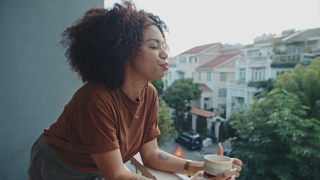 Latin Woman Drinking Cup of Morning Coffee and Looking at City from Balcony