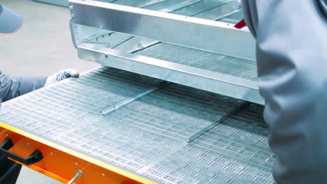los trabajadores ensamblan la rejilla de acero inoxidable en la máquina industrial