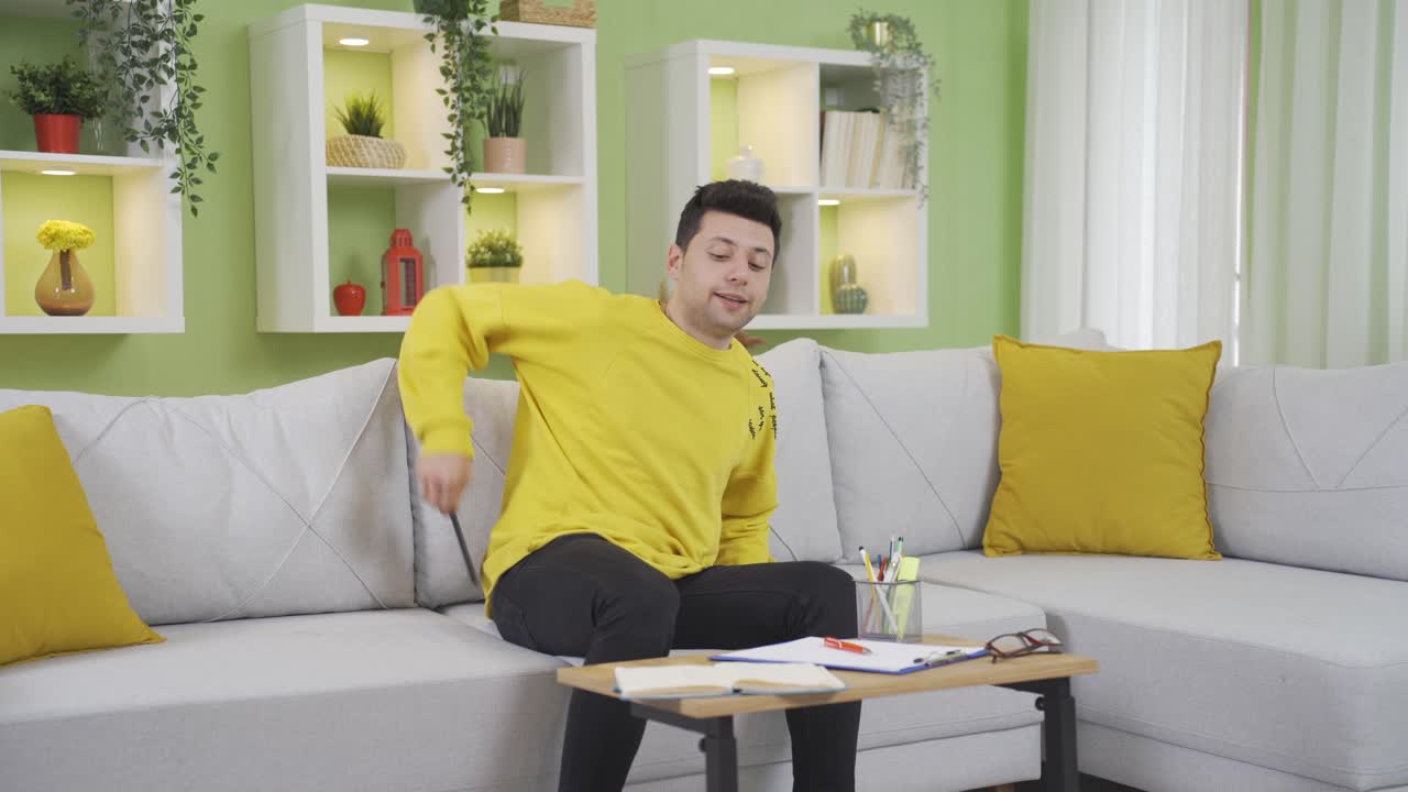 어색하고 사려 깊은 젊은이가 집에서 공부하는 동안 조정 가능한 책상을 해체하고 물건이 그 위에 떨어집니다.