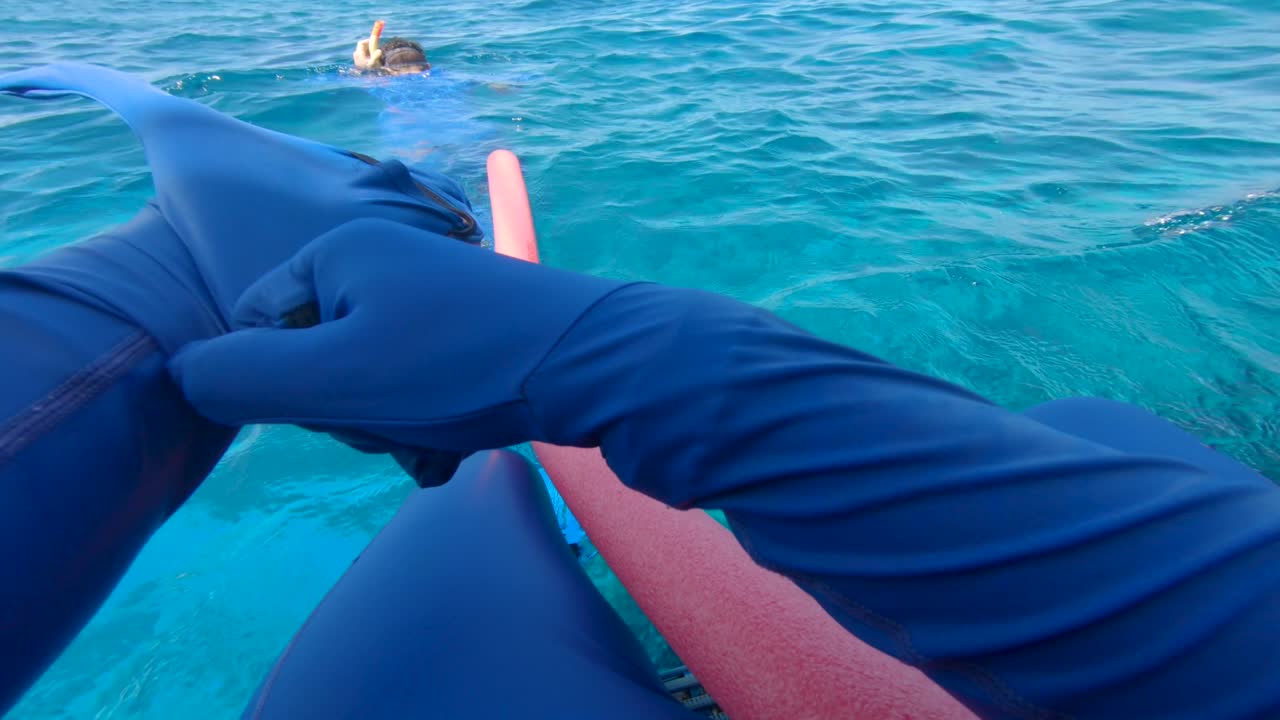 Man putting swim suit on and jumping in blue waters with swim noodle