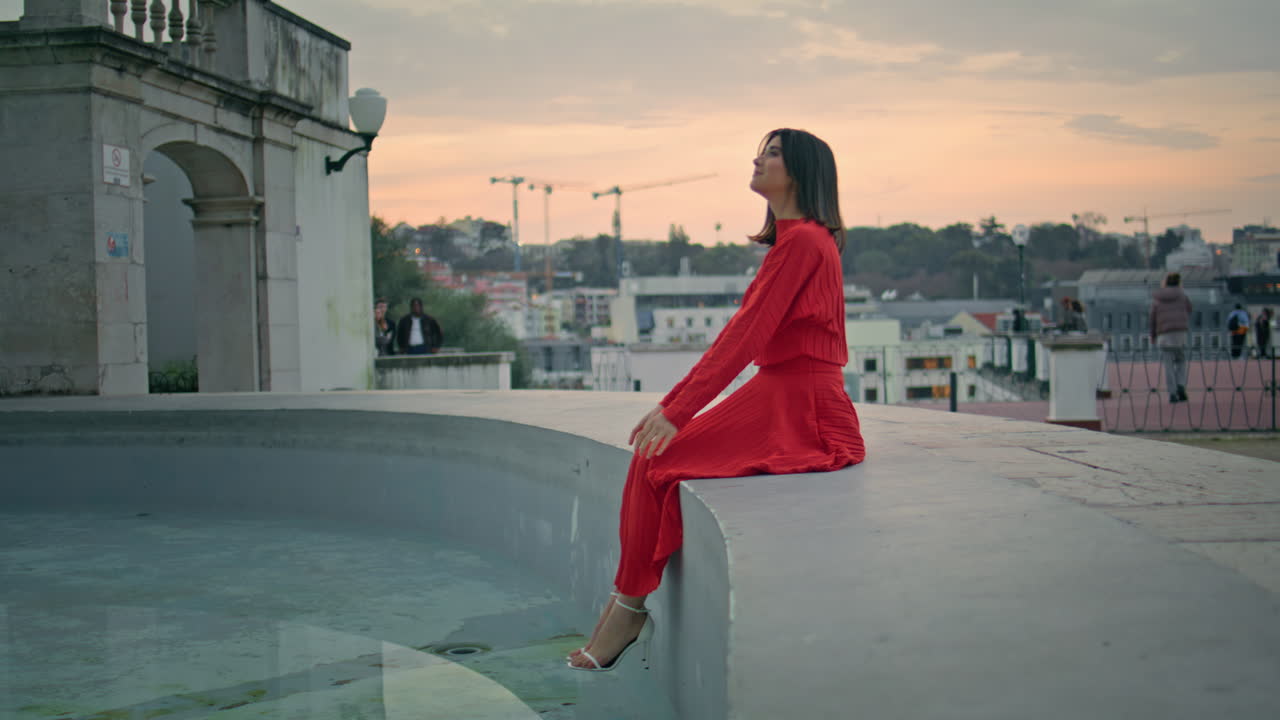 Feminine brunette resting fountain boarder at sunset city. Woman looking water