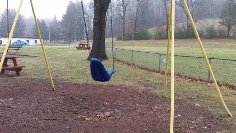 deserted playground swings swinging empty and lonely on a rainy and dreary day with motion