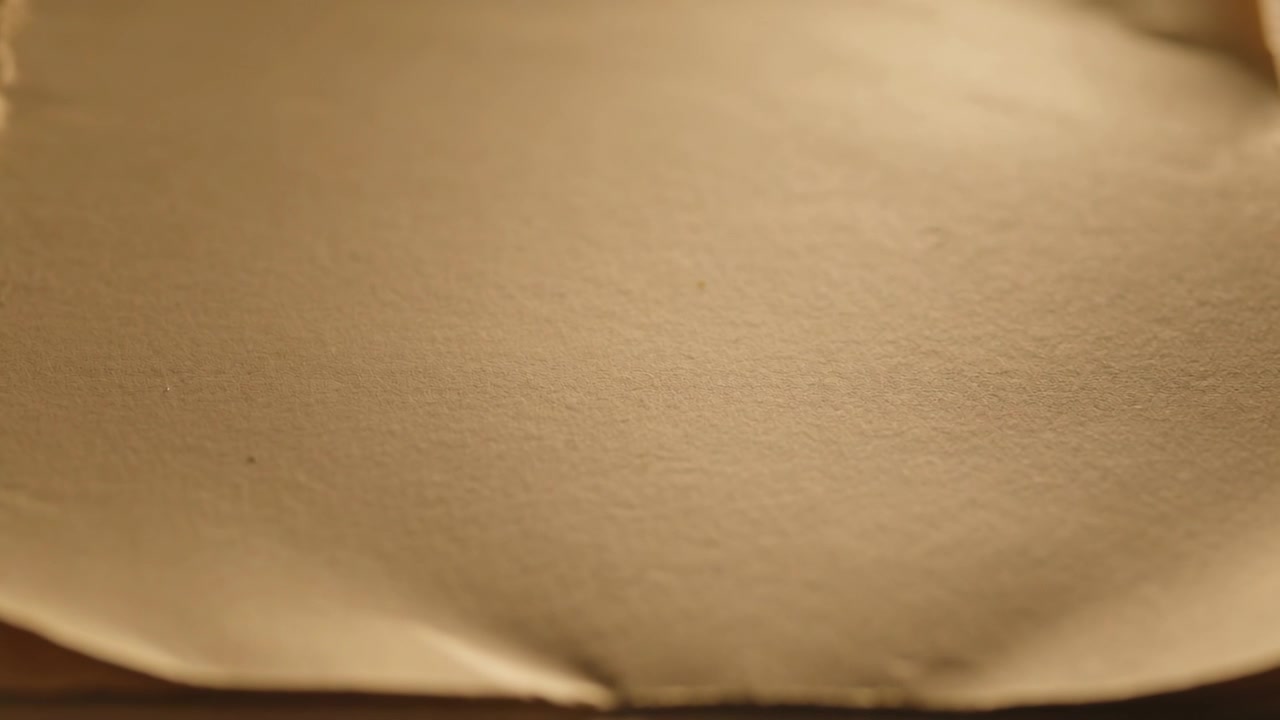 Luce calda e brillante dall'alto a destra che accarezza un foglio beige che si leviga su un vassoio con bordo, con il bordo sinistro strappato visibile.