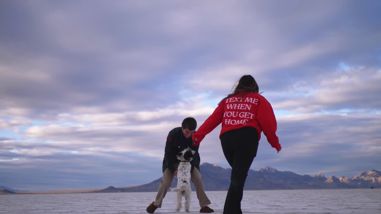 two lovers and their dog run around in the salt flats during sunset