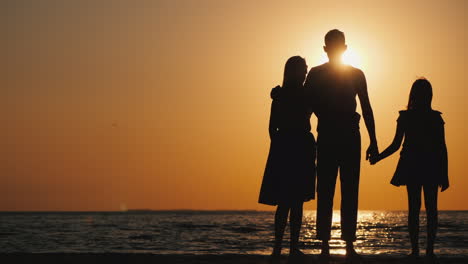 A-Young-Family-With-A-Child-Cuddles-And-Looks-Forward-To-The-Sunset-Over-The-Sea-Good-Time-Together-