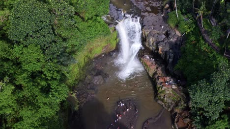 top-down view of tegenungan waterfall natural pool with tourists swimming and standing - bali, indonesia