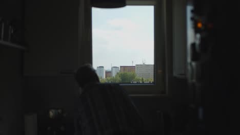 Man-looking-out-of-the-windows-to-block-of-flats-dark-kitchen-4K