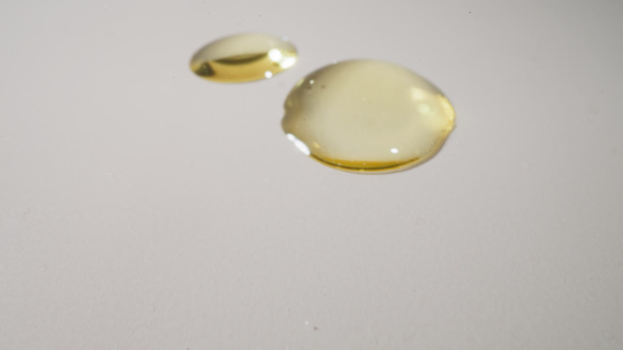 gotas doradas de aceite de jojoba que caen sobre una superficie blanca y lisa