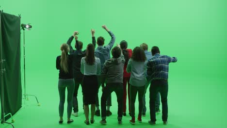 green screen chroma key studio: diverse row of seven fans cheering, jumping and applauding with hands in the air at the public sport event, concert, festival, party. back view full shot. slow motion