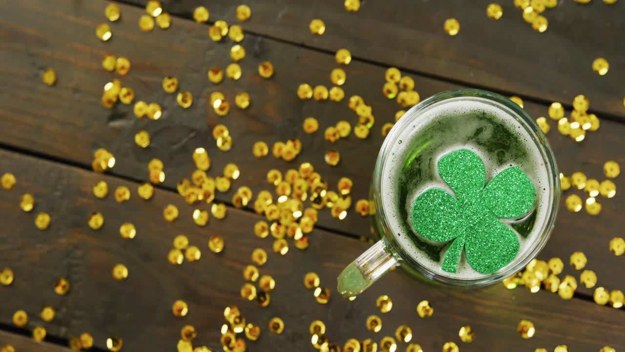 Video of st patrick's green shamrock in beer glass and gold sequins on wooden background