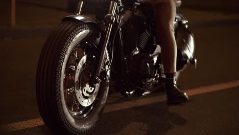 Close-up-of-steel-chrome-wheels,-a-motorcyclist-drives-a-bike-in-the-night-city,-waiting-traffic-light