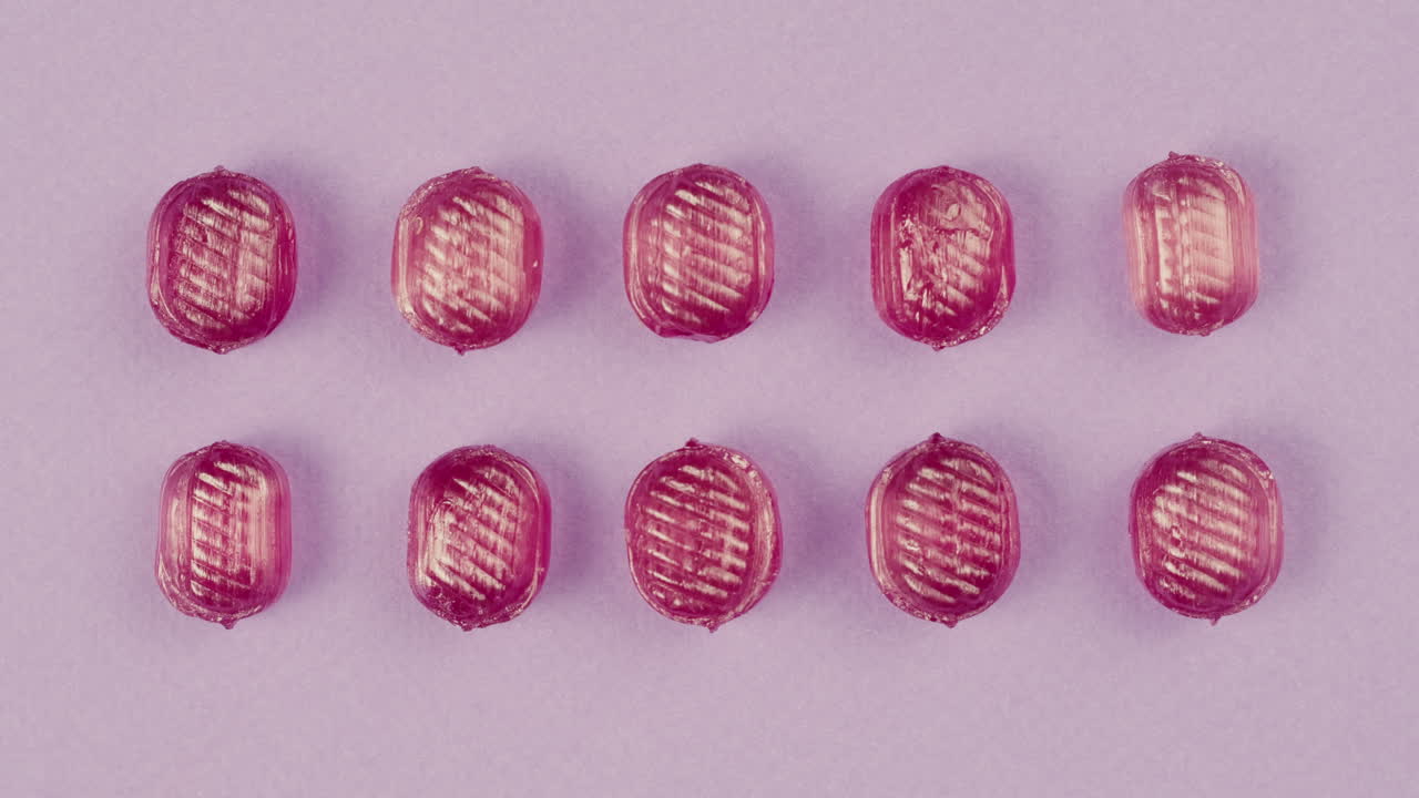 Pink lollipops, candies, bonbons disappear on purple background. Summer bright texture studio shot for store, supermarket, close up top view. Children's favorite sweets made of sugar.