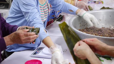 보라색 쌀과 고기 혼합물을 측정하고 준비하는 바쁜 주방 근로자의 손이 부엌의 잎 안에 싸여 있습니다.
