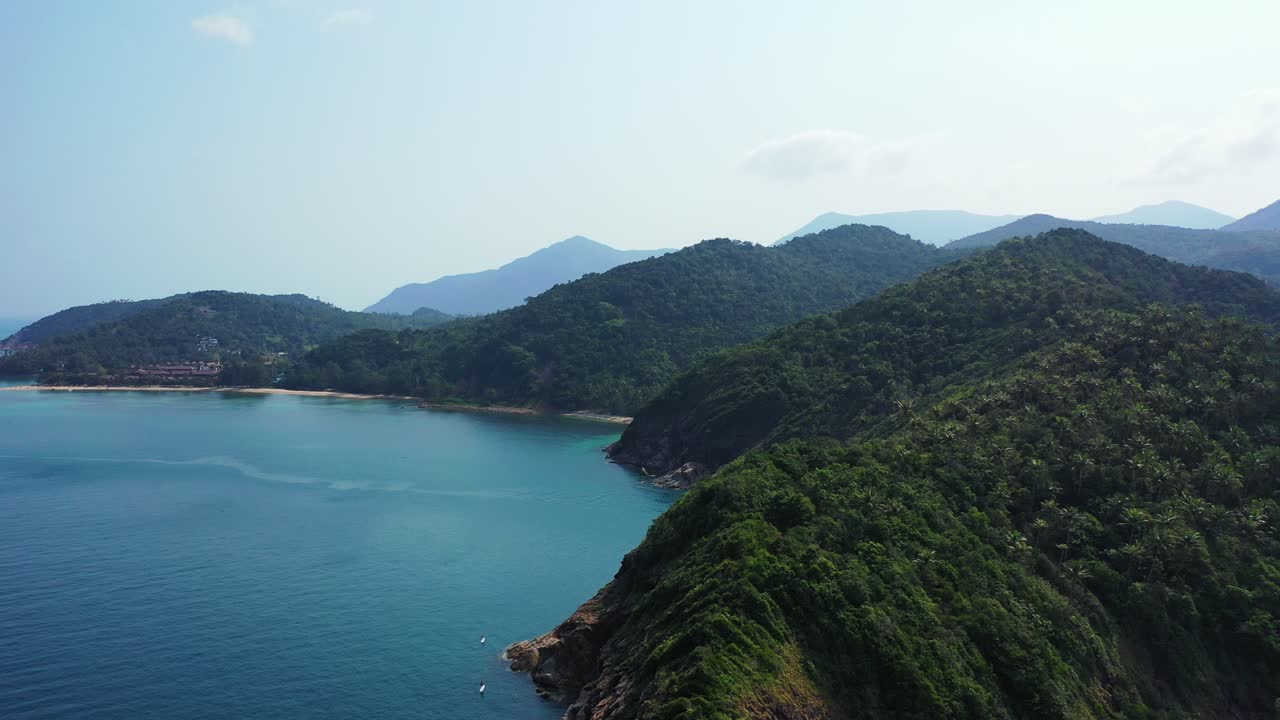Mountains of tropical islands with lush vegetation and rocky shoreline washed by calm sea surface reflecting sunlight, Thailand