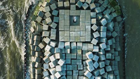 aerial birdseye view of protective stone pier with concrete blocks and rocks at baltic sea coastline at liepaja, latvia, strengthening beach against coastal erosion, drone shot moving back