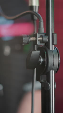 Close-up of a microphone stand in a studio room with colored lights in the background. The image captures the details of audio equipment in a professional recording environment