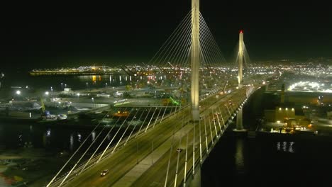 Aerial-orbiting-shot-of-lit-bridge-in-Long-Beach-California-|-Shipping-port-in-background