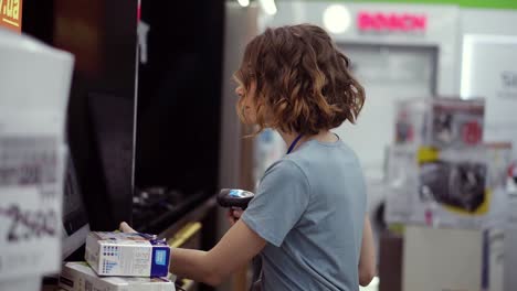 Curly-haired-concentrated-woman-seller-consultant-in-household-department-carry-and-scan-by-barcode-stationery-goods-in-the