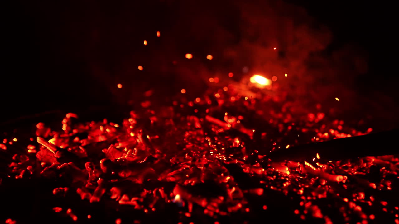 Hot smoldering red embers are moved by the stick. Bright sparkles flying up in the air. Black backdrop.