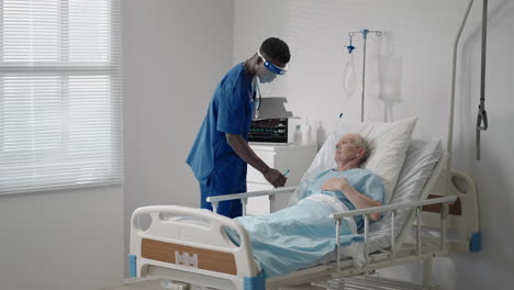 a black man cardiologist doctor is talking to an old man patient lying on a hospital bed discussing rehabilitation after recovery. an infectious disease neurologist discusses a treatment strategy