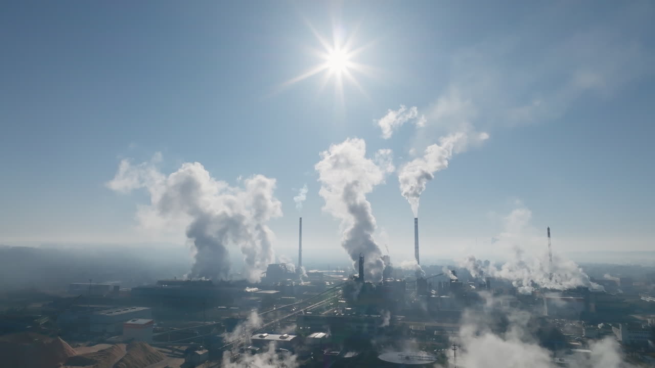 Ampia vista aerea su un vasto paesaggio industriale a Štětí, con alte ciminiere che emettono vapore e foschia atmosferica che ammorbidisce l'orizzonte lontano.