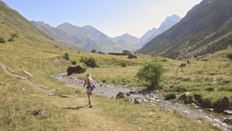 Mujer-Rubia-Caminando-Junto-A-Un-Pequeño-Arroyo-En-Benasque,-España,-Tiro-Panorámico