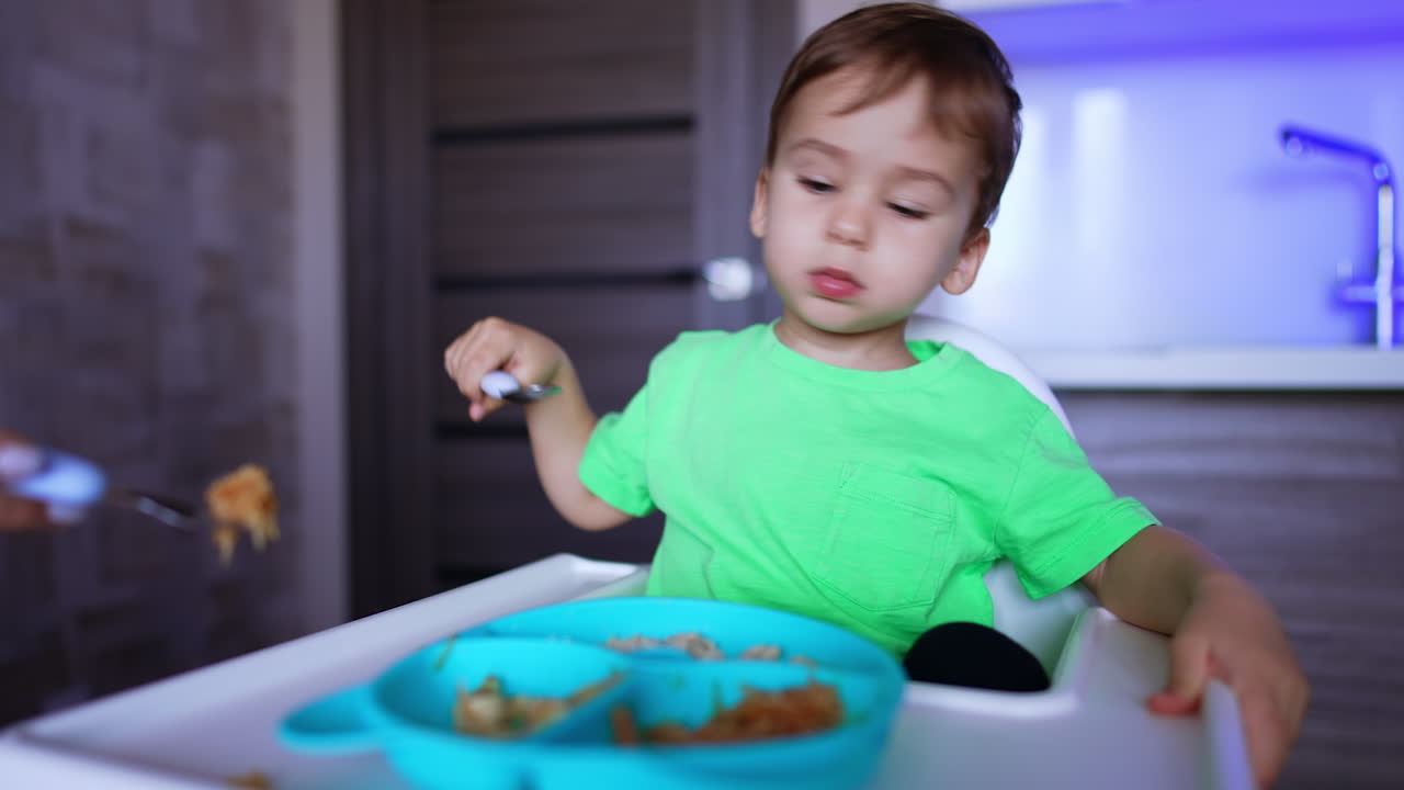 Adorable baby boy waves his head refusing from food. Mother tries to feed her child but fails.