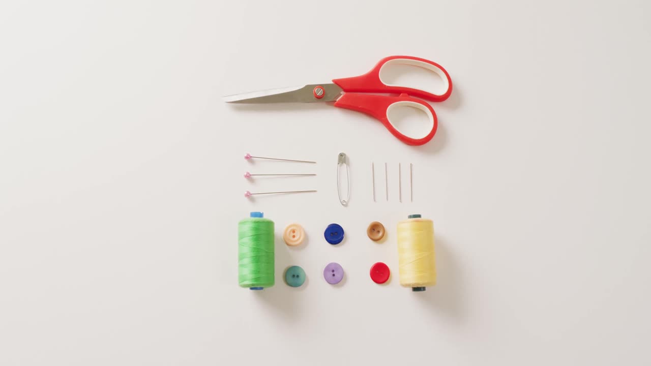 Video of scissors, buttons, pins and cotton reels arranged on white background