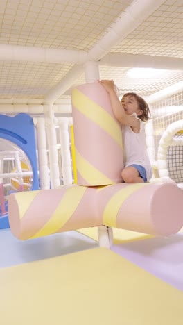 a young toddler girl is happily being spun on a large, soft, marshmallow-shaped ride with pink and yellow stripes in a vibrant indoor playground, enjoying the motion - sloqw motion