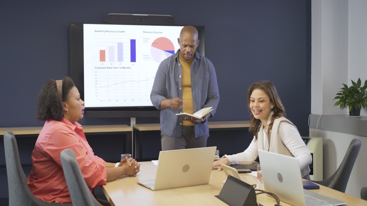 Diverse coworkers in office analyzing charts on screen reading data passing docs and laughing