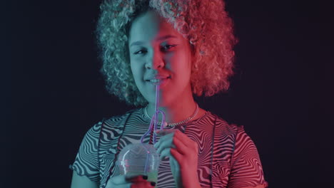 young woman drinking a drink under neon lighting