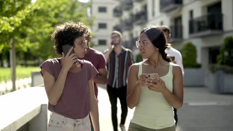 cheerful young women talking and using smartphones on street