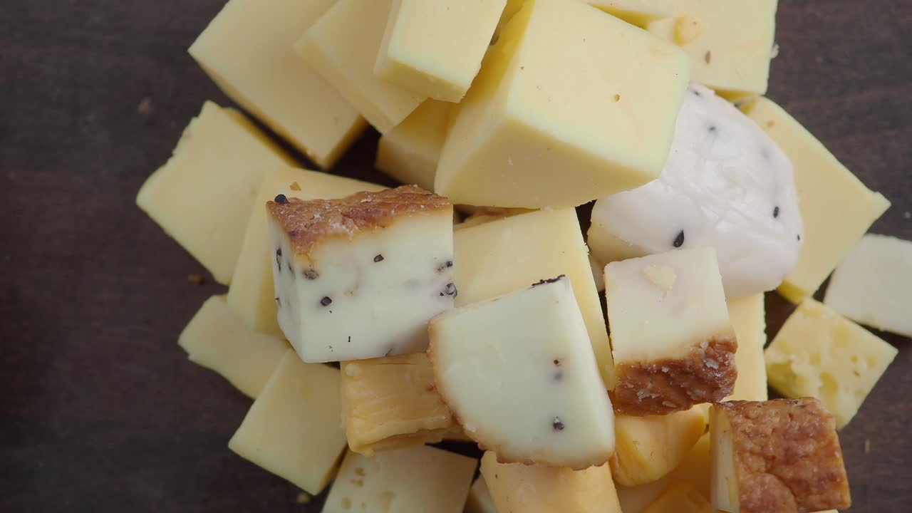 Assortimento di cubetti di formaggio e una forma di formaggio su un tagliere di legno.