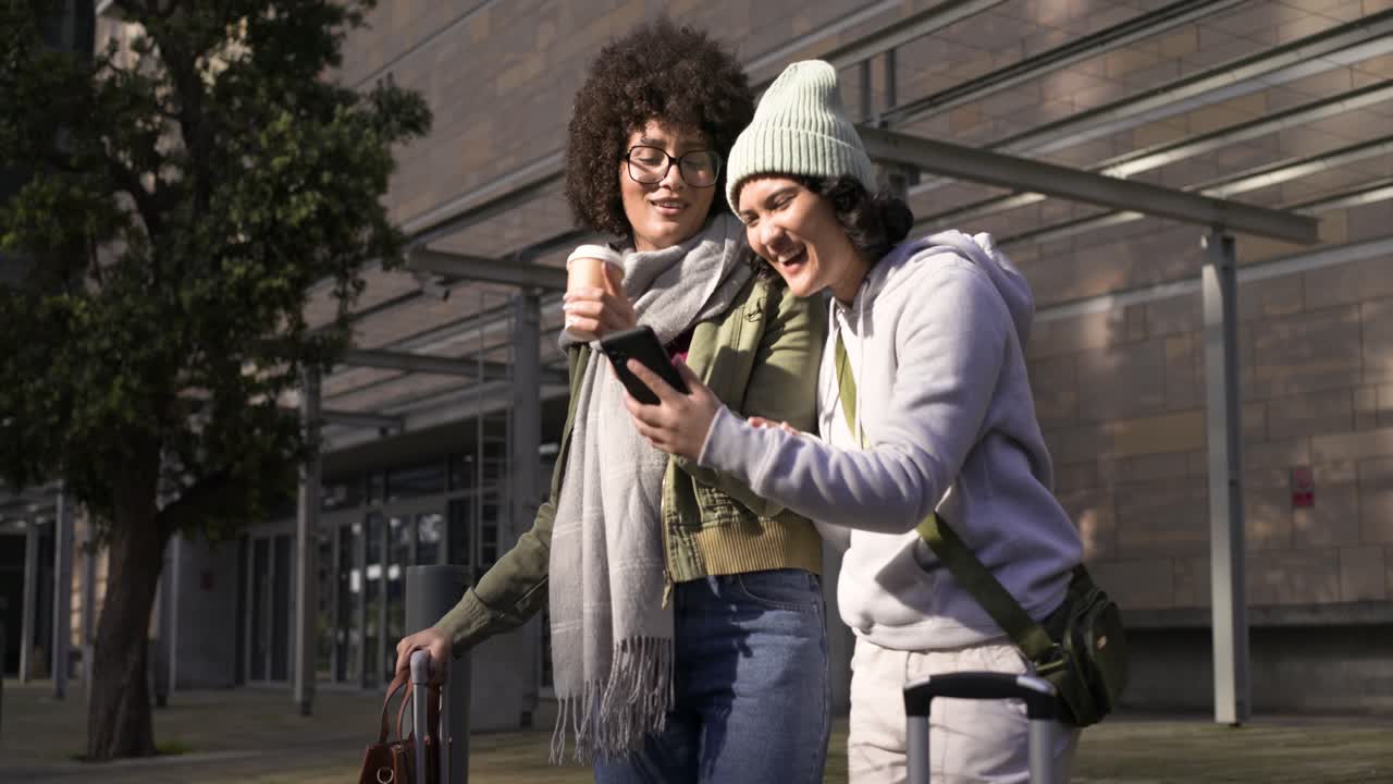 Diverse amiche in pausa in piazza controllano i selfie, sorseggiano caffè e camminano con una valigia.