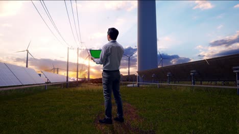 full body back view of an asian male professional worker standing with green screen tablet with solar panel and wind turbines, industrial facility