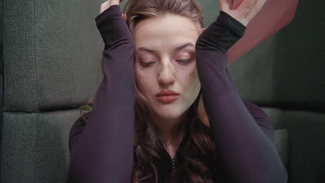 woman with brown wavy hair wearing black top writes in notebook while leaning forward on table with thoughtful expression in quiet setting, showing emotion and focus during reflective moment