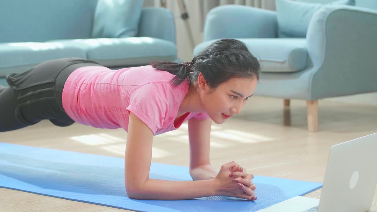 mujer asiática haciendo plancha de yoga y viendo tutoriales en línea en la computadora portátil, entrenamiento en la sala de estar