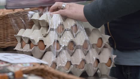 comerciante envolviendo cartones de huevos de pollo con película para un cliente en el mercado local