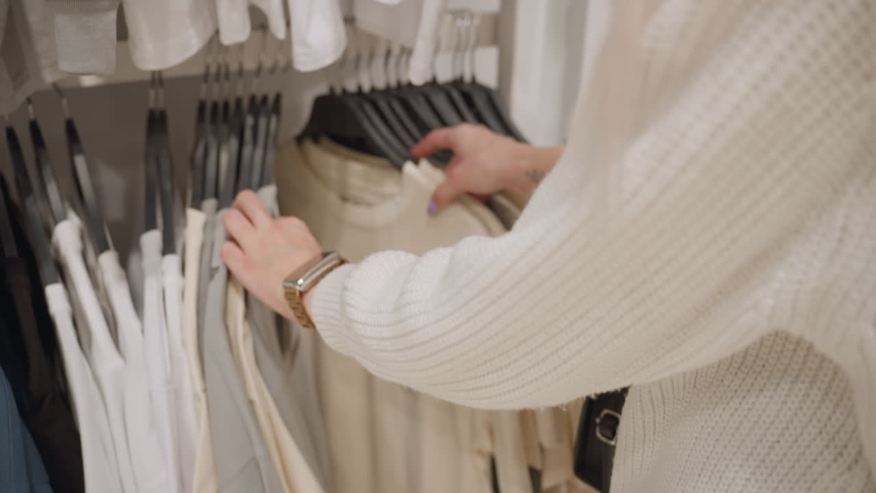 Expectant mother in chunky knit sweater and denim jeans stands before color sorted polos on hangers, scanning subtle hues, deciding comfortable maternity friendly top while resting hand near belly